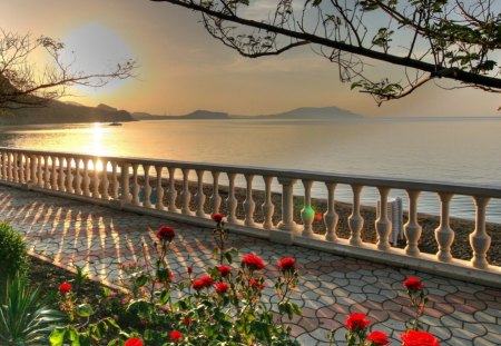 Splendid view of the ocean - red, railing, water, flowers, stones, brillant sun, ocean, plants, trees, sunset, walkway, balcony