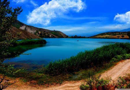 Pathway Around Lake - sky, trees, water, dirt, path, road, white, brown, clouds, green, grass, lake, mountain, day, bushes, nature, blue, leaves