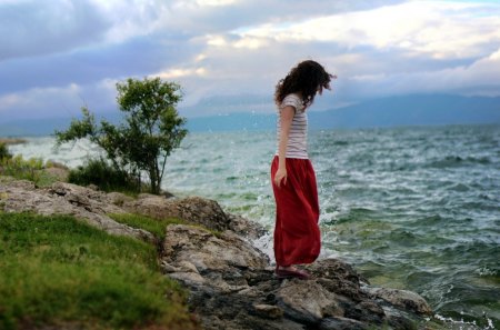 On the Edge - woman, beauty, sky, ocean waves, female, hair, rocks, storm, hand, clouds, green, stormy, grass, hands, lady, ocean, girl, lovely, waves, nature, beautiful, splendor, colors, sea, dress