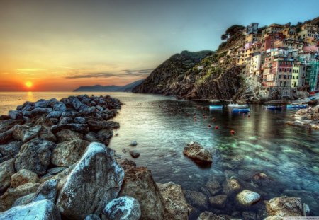 Sunset at the End of the Day - ocean, sky, houses, mountain, day, sun, water, sunset, rocks, nature, yellow, clouds, blue, architecture, orange