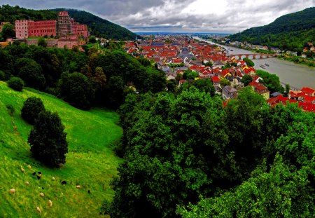 View to the town - nice, sky, slope, trees, roofs, riverbank, greenery, water, view, pretty, clouds, river, green, grass, bridge, houses, lake, mountain, hills, summer, lovely, nature, village, town, red, beautiful, europe