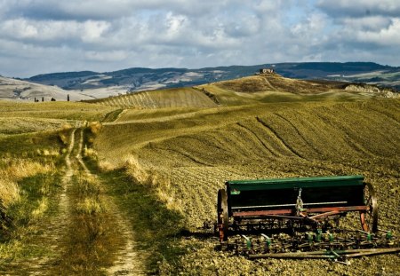 rural scene in tuscany - road, clouds, harvester, fields