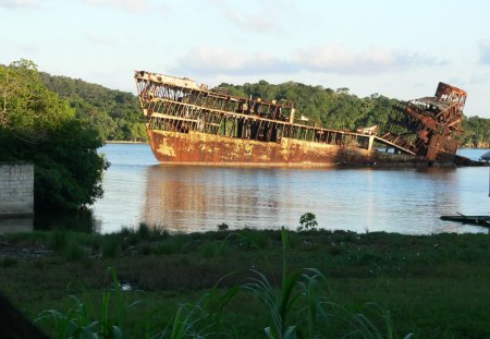 This boat has seen better days - sky, trees, bank, river, old boat, grass