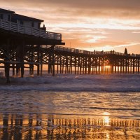 waves crashing under pier at sunset