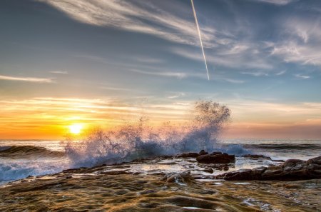 wave breaking on rocky shore at sunset - sunset, shore, plane trail, sea, wave, rocks