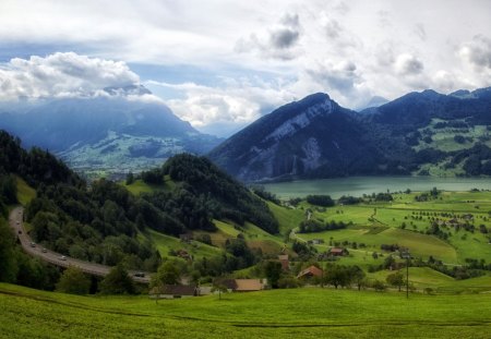 beautiful landscape to a mountain lake - village, clouds, highway, lake, meadow, mountains