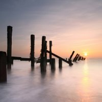 sunrise over an old pier in a misty sea