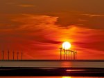 row of turbine windmills offshore at sunset