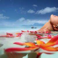 Tahitian Girl relaxes in blue lagoon in Tahiti with plumeria frangipani flowers