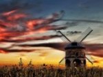 windmill in a field under fiery skies