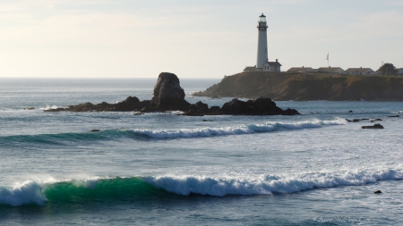 lighthouse above turqoise waves on a rocky beach - haze, lighthouse, beach, waves, sea, rocks