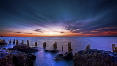 dawn over old pylons at the seashore - clouds, dawn, shore, pylons, sea, rocks