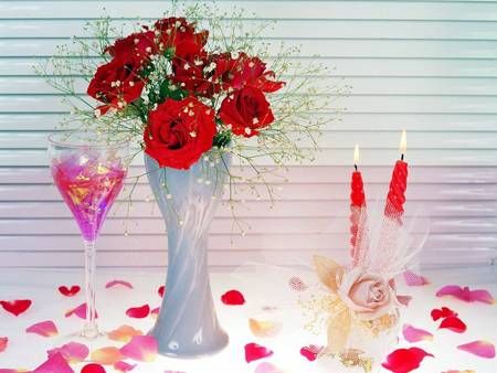 Romantic setting - rose petals, candles, champagne flute glass, vase of red roses