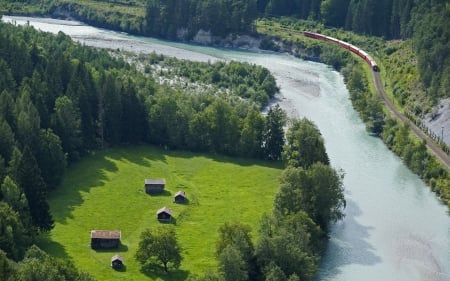 view of a train running along a river - river, train, tracks, trees, view, grass, houses