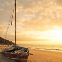 a beat up old sailboat on a beach at sunrise