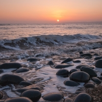 sea waves over smooth beach stones at sunset