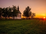 little chapel on a grassy hill at sunset