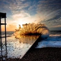 waves crashing on a beach pier at sunset