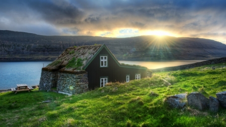 stone cabin with a grass roof by a river at sunset hdr