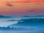 misty blue tuscan landscape under orange sky