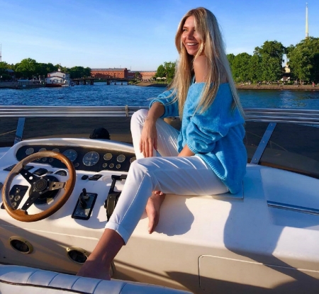 Anjelica Ebbi enjoying a boat ride - water, coast, boat, pale blue sweater, blonde, revealing left shoulder, steering wheel, instrument panel, white capri pants, sitting