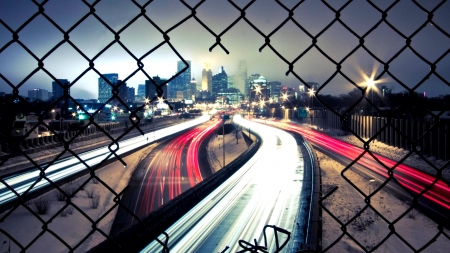 View of city freeway through cut fence during winter - fence, car, night, city, freeway, winter, crafted, road