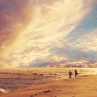 Surfer couple walking up a pleasant beach at sunset