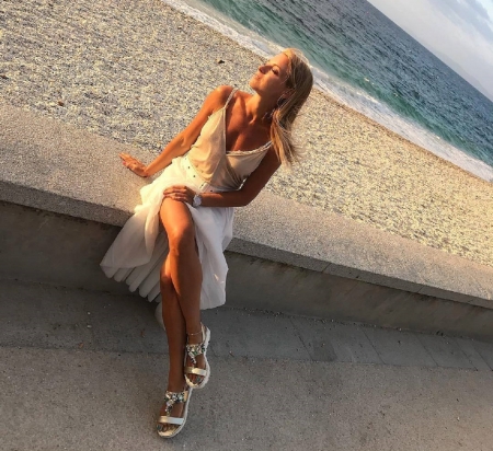 Francesca Leto - belt, white skirt, spaghetti straps, blonde, coloured studs on sandals, beige top, beach scene, sitting on wall