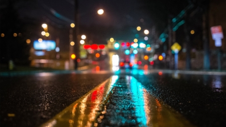 A downtown road covered in rain, glowing from nearby traffic lights