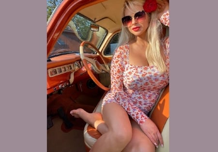 Paula Tumala - short white dress, red rose in hair, red flower pattern, platinum blonde, posing on drivers side of car, sunglasses