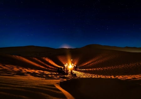 People camping around a fire in a desert during a clear night