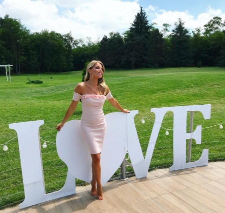 Francesca Leto - trees, bare feet, off shoulder, blonde, white electric lights, large green area, lage round earrings, pale pink dress, neckline with matching roses, love sign