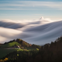 A home sitting atop a lush mountain encircled by soft-serve clouds