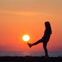 Girl kicking at the sun by the beach at sunset