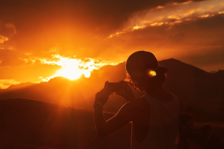 Casually-dressed man takes a picture of a mountain sunset on his phone - mountains, sun, sunset, golden, photography, man, hot, golden hour, gold, photographer, clouds, warm, sky