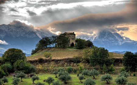 House On A Hilltop Below The Mountains - hill, clouds, house, trees, hills, grass, mountain, skies, green, old, plants, field, mountains