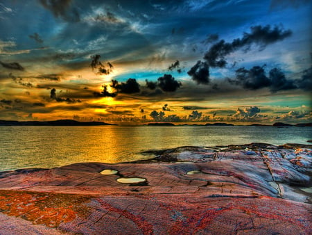 Scrambled sky - clouds, water, blue, gold, dark, aqua, black, shore, sunset, sky, rocks