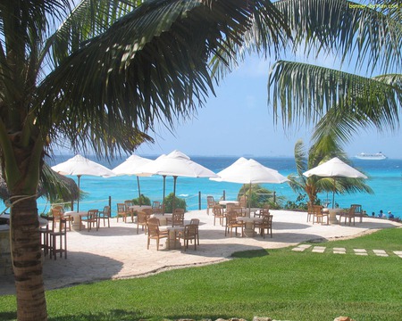 Tropical Getaway - ocean, trees, palms, paving, water, chairs, path, tables, umbrellas, ship, blue, island, holiday, grass, sea