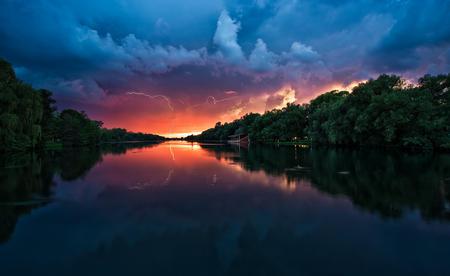 Before the Storm Begins - yellow, summer, blue, spring, pink, reflection, plants, lake, lightning, cloudy, sky, sun, storm, clouds, trees, water, sunshine, orange, river, sunset, green, gray